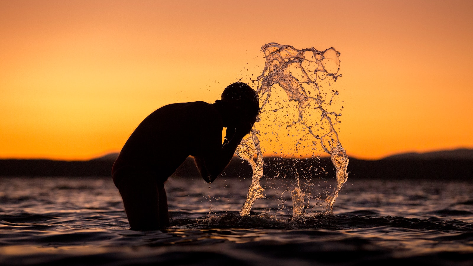 silhouette of man washing his face on body of water