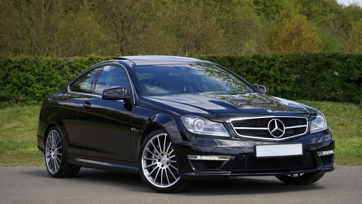 Luxurious black Mercedes Benz coupe parked on a scenic outdoor setting with lush greenery.