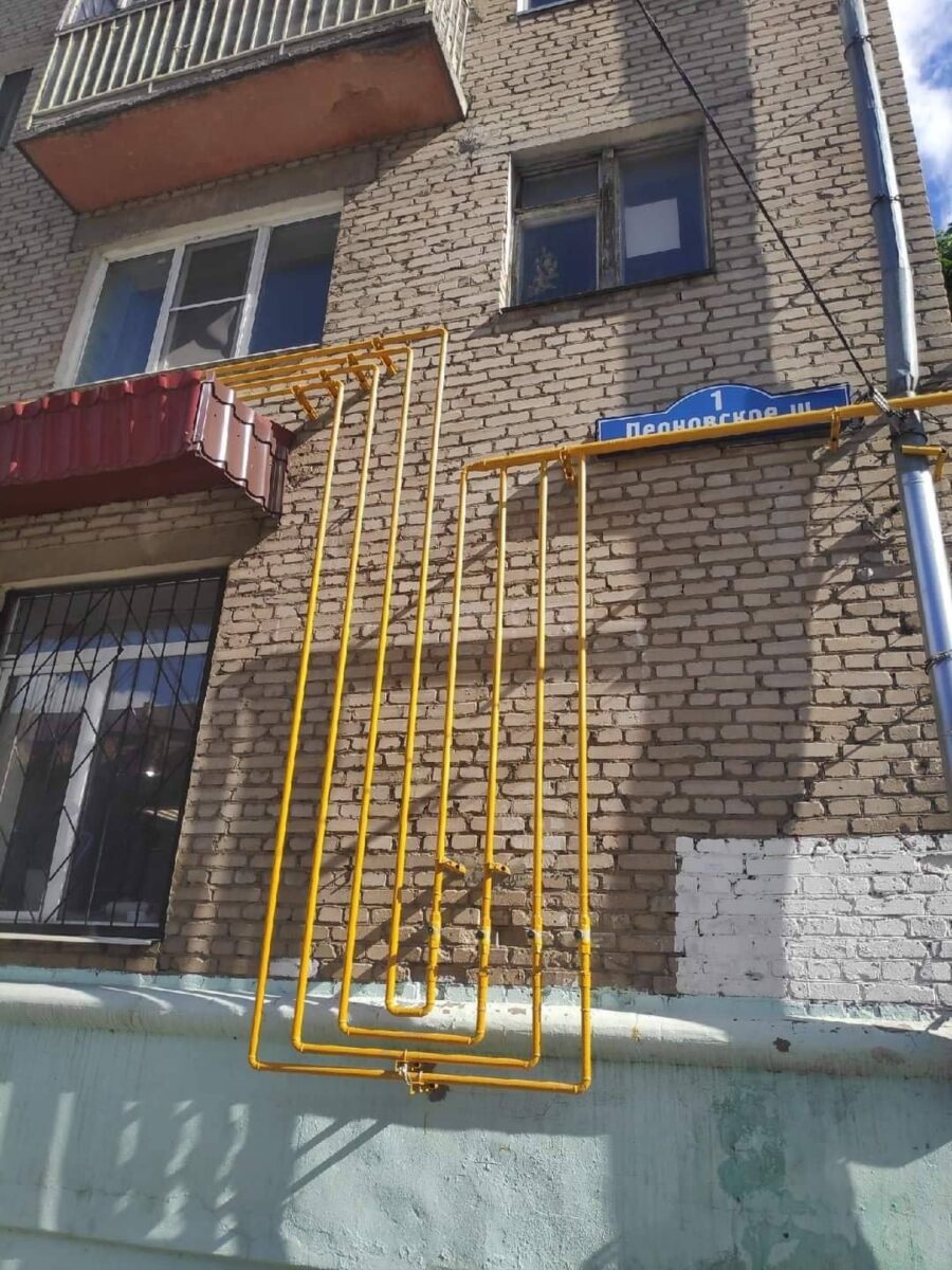 Žlté potrubie s niekoľkými pravouhlými ohybmi na tehlovej fasáde domu.