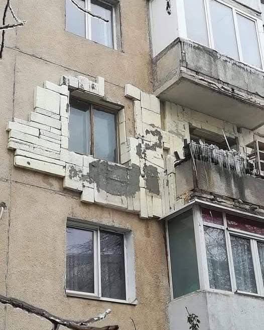 Fasáda bytového domu s rôznymi povrchmi a svetlými obdĺžnikovými dielmi okolo okien.