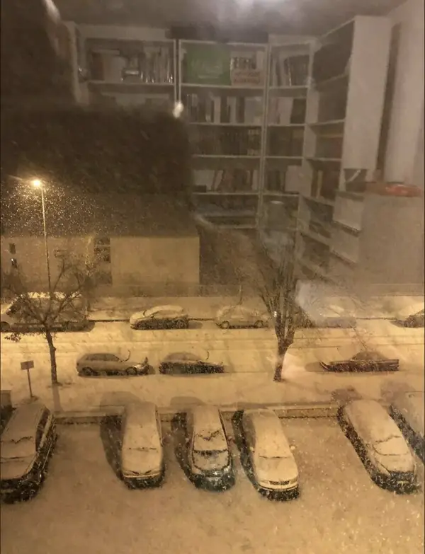Osvetlené police sa na okne prekryjú so zasneženou ulicou.