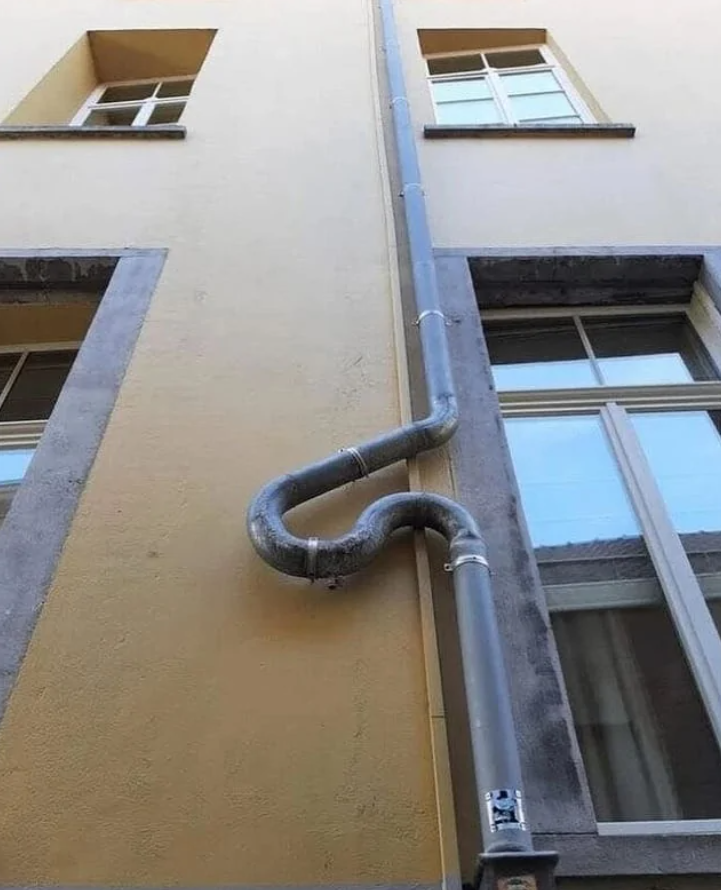 Zvodová rúra na fasáde s výrazným oblúkovým ohybom medzi oknami.