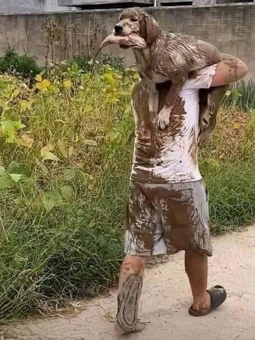 Človek nesie zablateného psa na pleciach; blato má aj na oblečení.