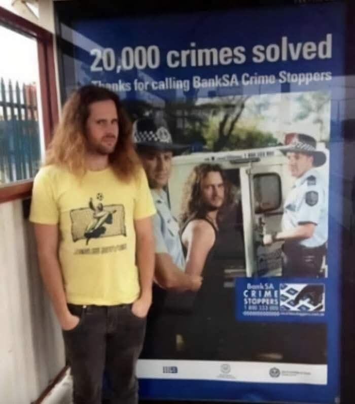 Človek s dlhými vlasmi stojí pred plagátom s podobnou postavou.