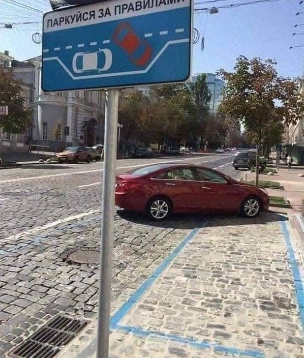 Tabuľa so schémou parkovania nad vyznačenými miestami a červeným autom