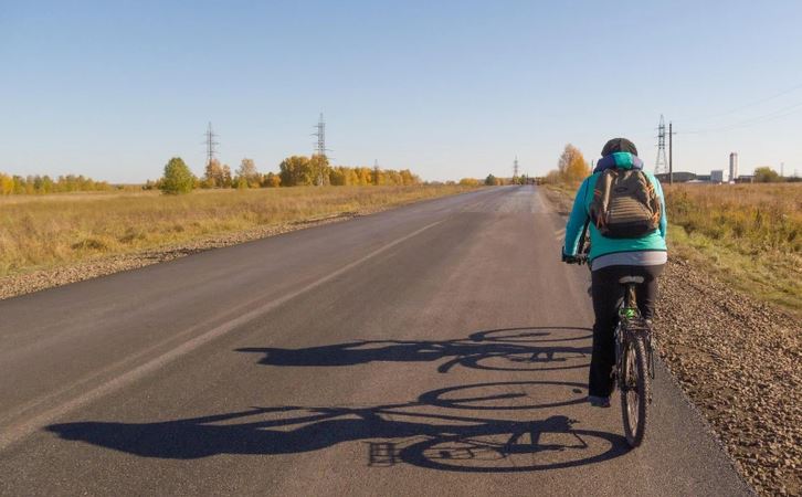 Cyklista na ceste v jesennom prostredí, obloha je jasná a na vidieku sú v diali stromy.