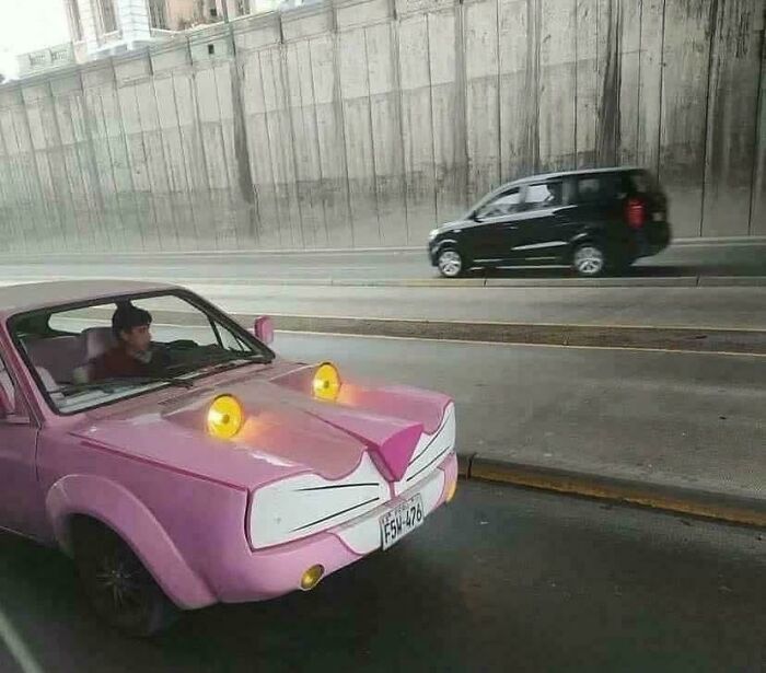 Ružové auto s dizajnom inšpirovaným animovanou postavičkou jazdí vedľa čierneho auta v tuneli.