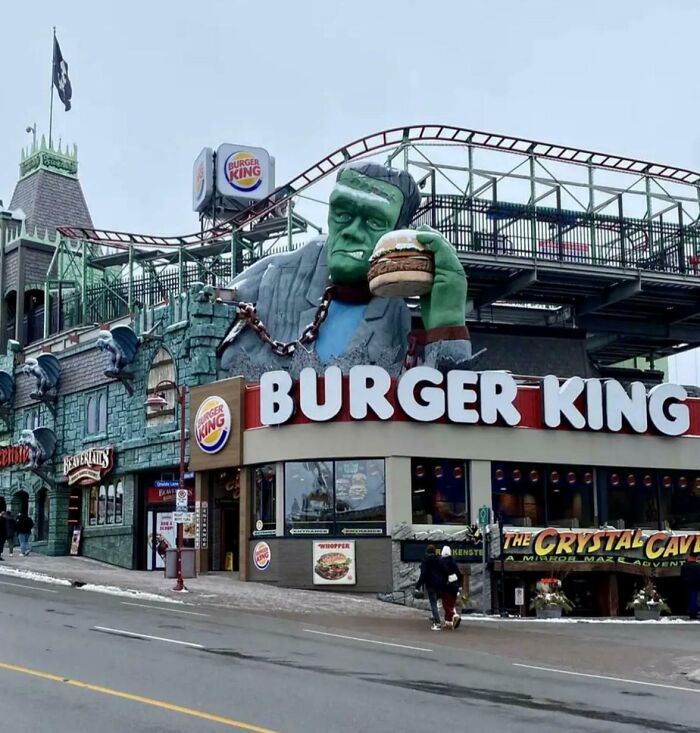 Obrovská socha monštra držiaca hamburger zdobí reštauráciu Burger King s horskou dráhou v pozadí.