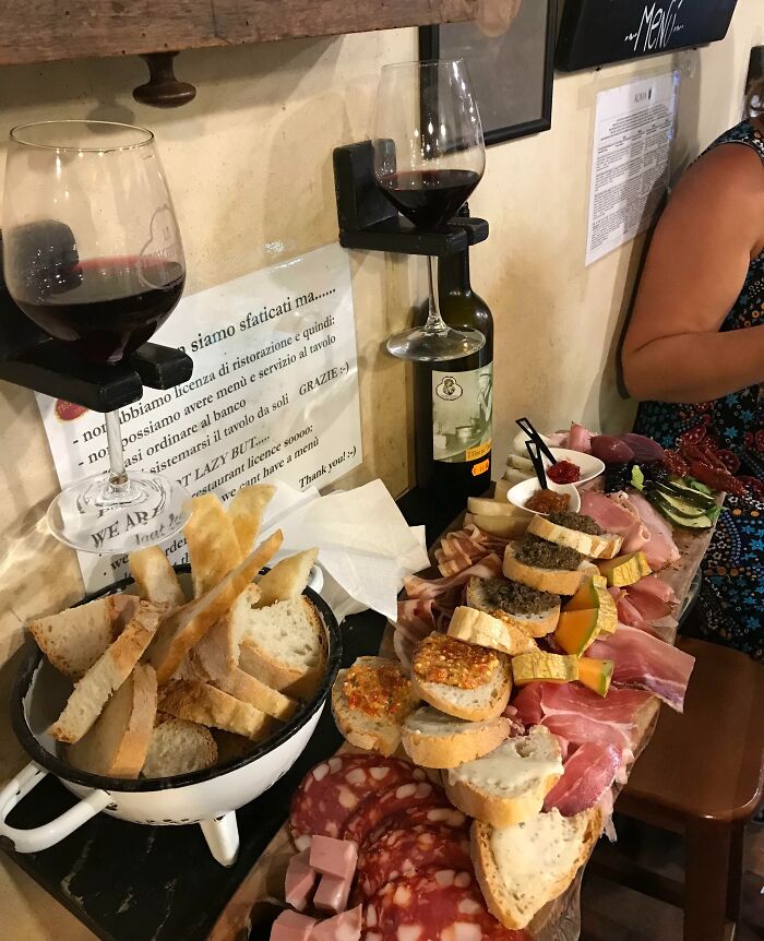 Tanier s antipasti, poháre červeného vína a košík s chlebom na drevenom stole v rustikálnej reštaurácii.