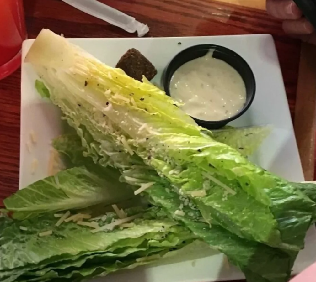 Šalát Caesar s rímskym šalátom, parmezánom a krutónmi na bielom tanieri s dipom na boku.