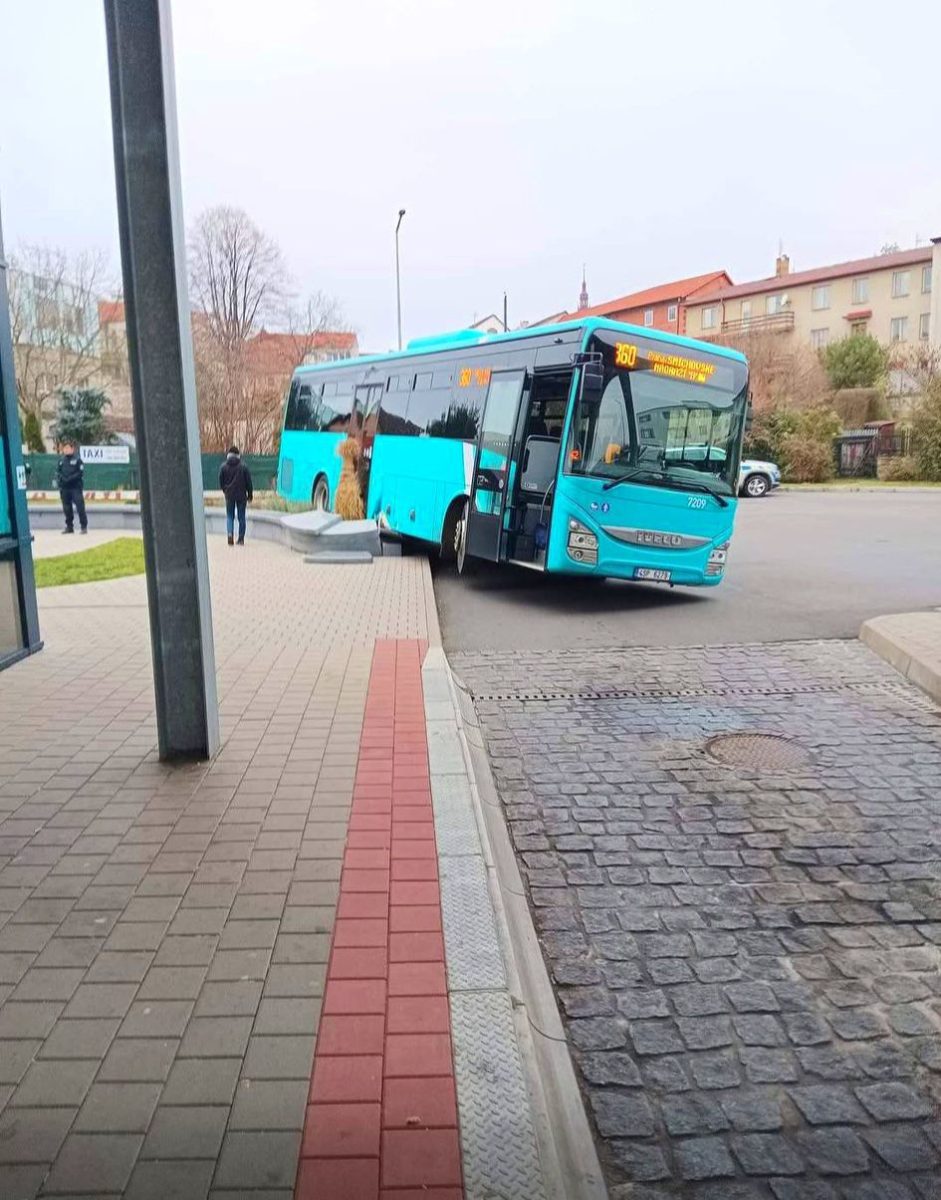 Tyrkysový autobus naklonený prednou časťou pri obrubníku.