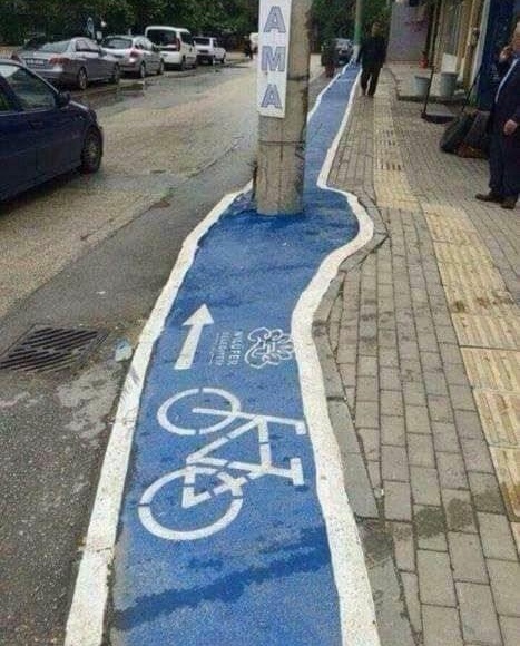 Modrý pruh so symbolom bicykla vedie okolo stĺpa na chodníku.