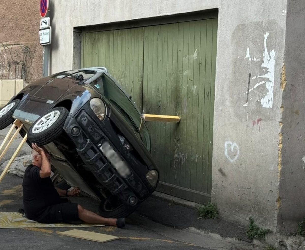 Naklonené auto pri garáži a človek pod ním s drevenou podperou.