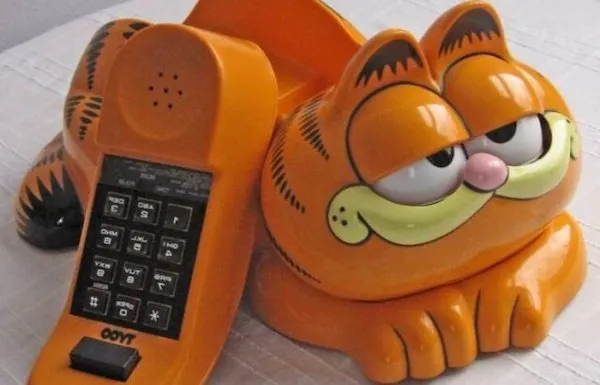 Oranžový telefón v tvare mačky s výrazom typickým pre Garfielda, ležiaci na bielej podložke.