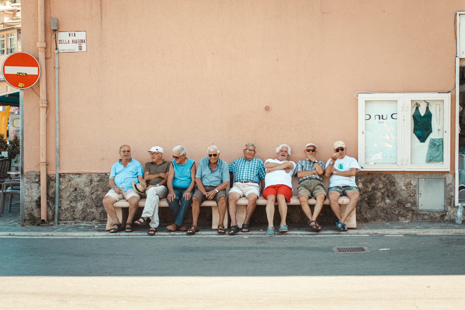 eight men sitting on bench near orange wall during daytime