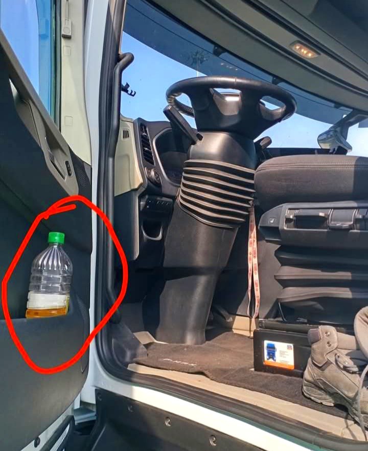 Plastová fľaša so žltou tekutinou pri volante pracovného stroja.