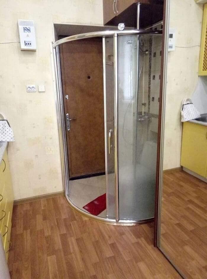 Sprchový kút neobvykle umiestnený v kuchyni s drevenou podlahou a žltými skriňami.