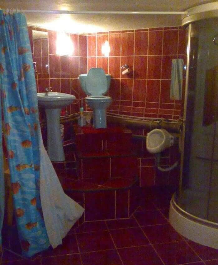 Kúpeľňa s modrým WC, umývadlom a sprchovým kútom na vyvýšenom podstavci, červené obklady.