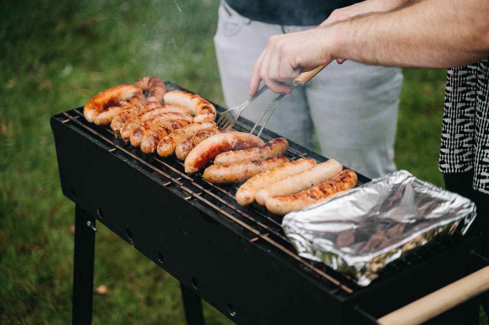 a man grilling hot dogs and sausages on a grill