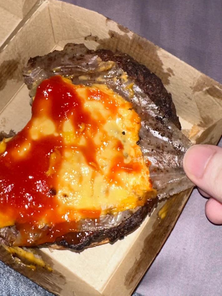 Burger so syrom a kečupom čiastočne olúpaný z obalu, pripravený na konzumáciu.