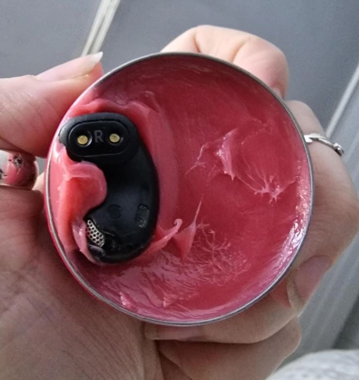 Slúchadlo zaliate v ružovom vosku v kovovej nádobe držanej v ruke, detailný pohľad.