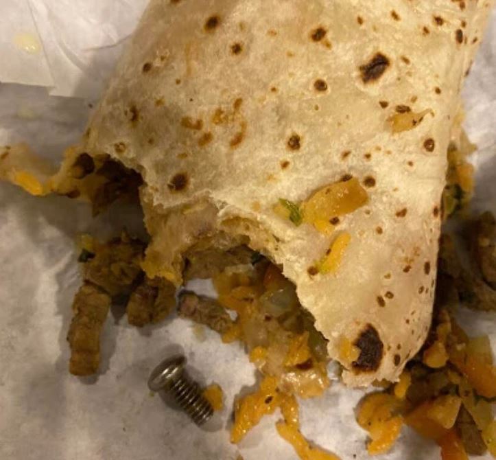 Burrito s roztrhnutým obalom, uvoľnená náplň a kovová skrutka na papieri vedľa jedla.