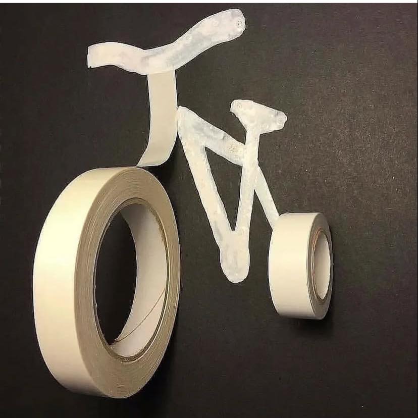 Pásky vytvárajú tvar bicykla na čiernom pozadí. Kreatívne využitie materiálu v umení.