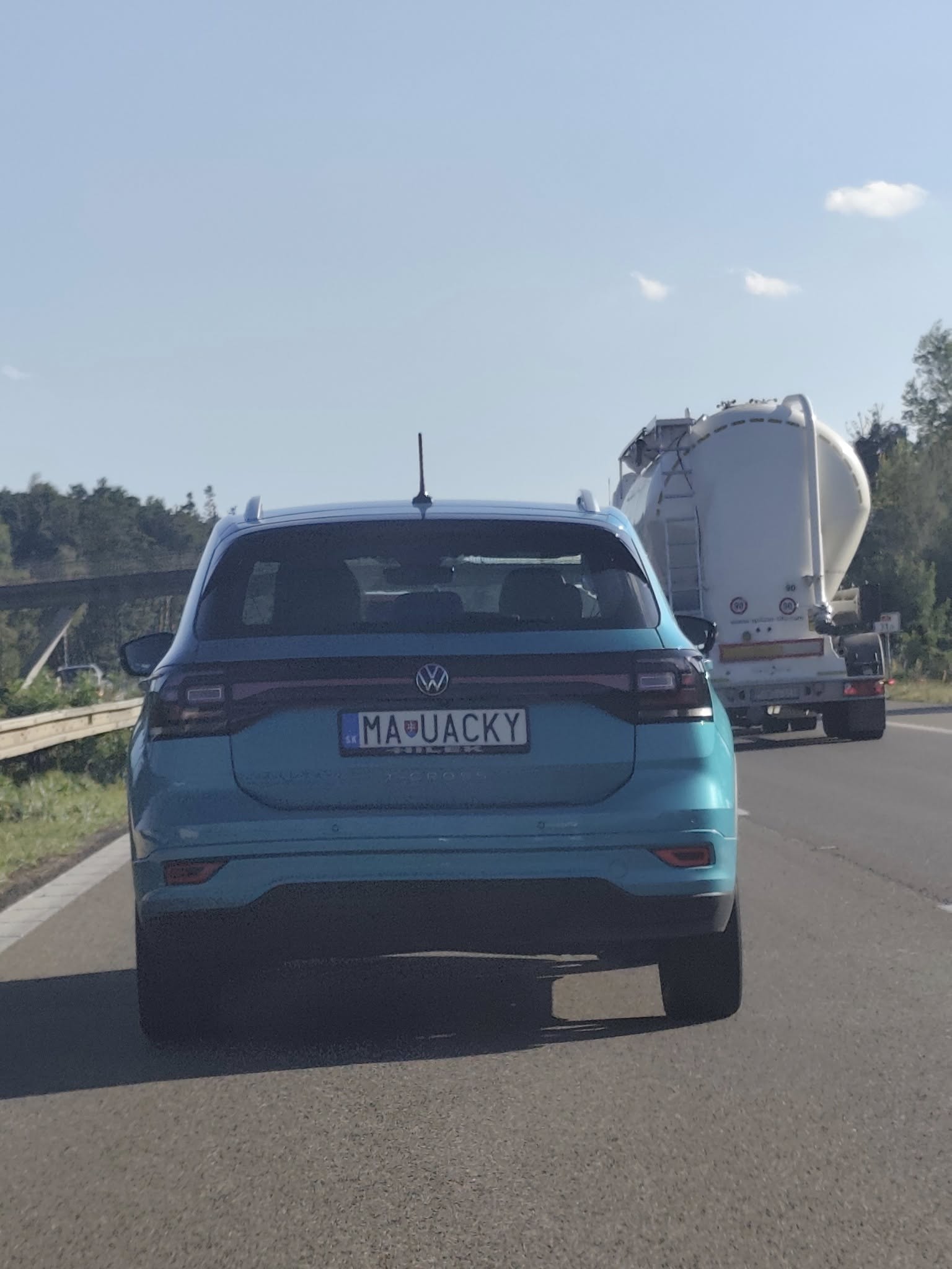 Modré auto Volkswagen na ceste vedľa bieleho nákladného automobilu za denného svetla.
