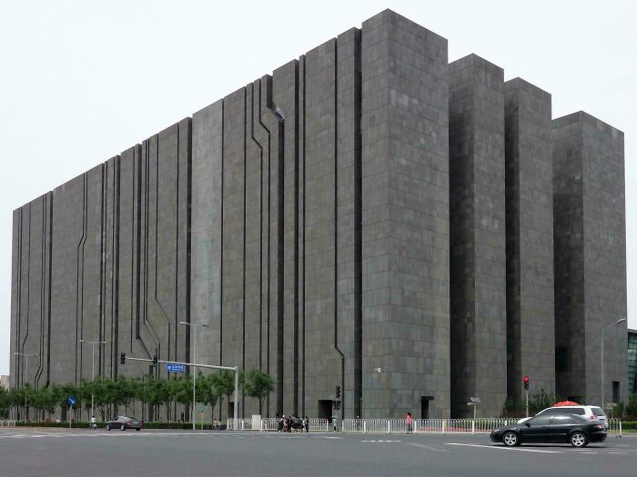 Veľká betónová budova s moderným architektonickým štýlom na rohu mestského bloku počas dňa.