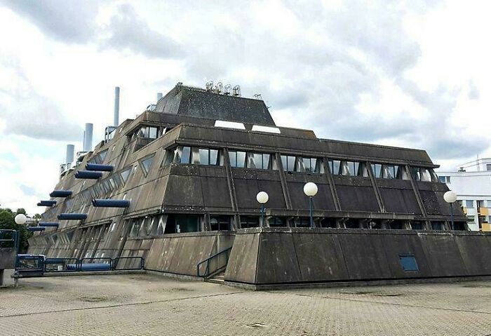 Brutalistická budova s geometrickým dizajnom a sivým betónovým exteriérom pod zamračenou oblohou.