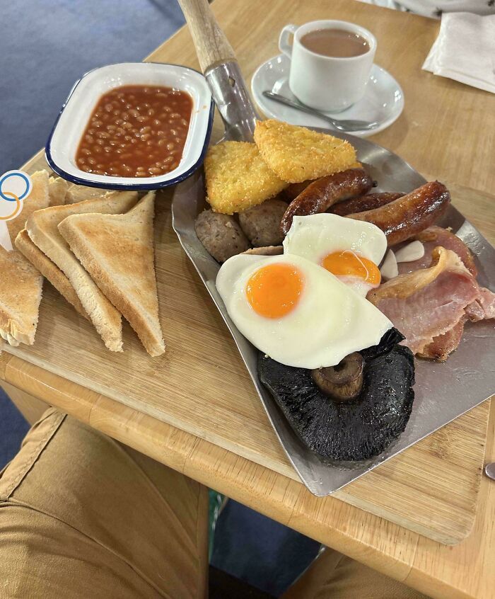 Tradičné anglické raňajky na lopate: vajcia, slanina, klobása, fazuľa, toasty, hash browns a čaj v šálke.
