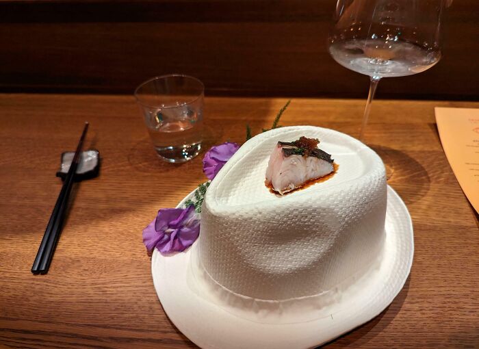Porcia sushi na bielom klobúku s ozdobnými fialovými kvetmi na drevenom stole.