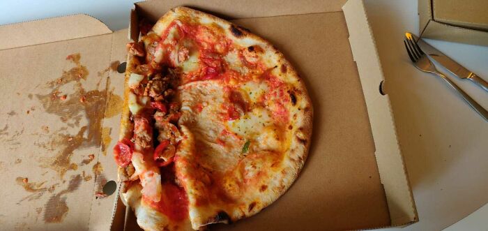 Pizza v krabici s nezvyčajne presunutými ingredienciami na jednu stranu.