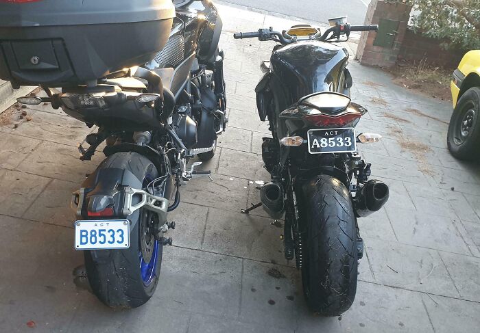 Dve zaparkované motocykle vedľa seba na chodníku so zreteľnými poznávacími značkami.