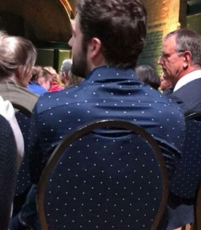 Muž v bodkovanej košeli sedí na bodkovanej stoličke v publiku.
