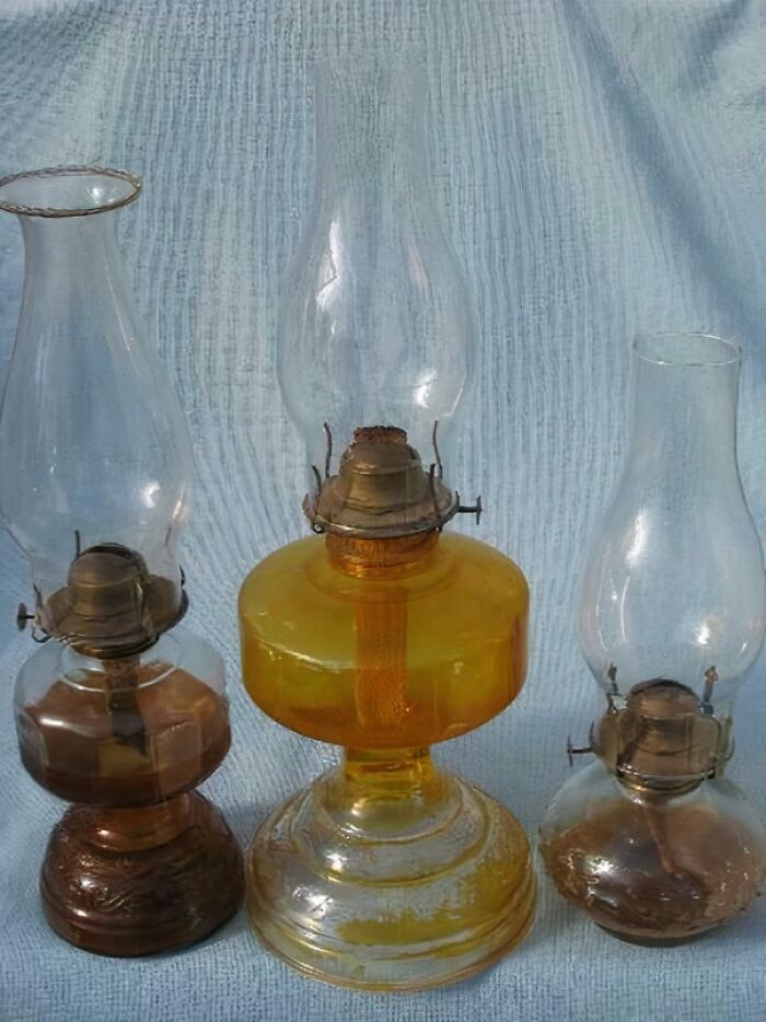 Tri vintage petrolejové lampy s farebným sklom na bielom pozadí.