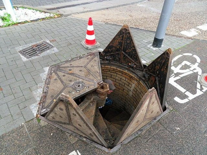 Otváracie dvierka nad schodiskom do podzemia označené dopravným kužeľom na chodníku v meste.