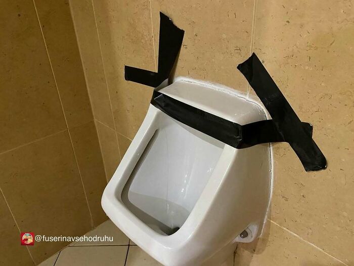 Pisoár pripevnený lepiacou páskou na béžovej kachľovej stene.