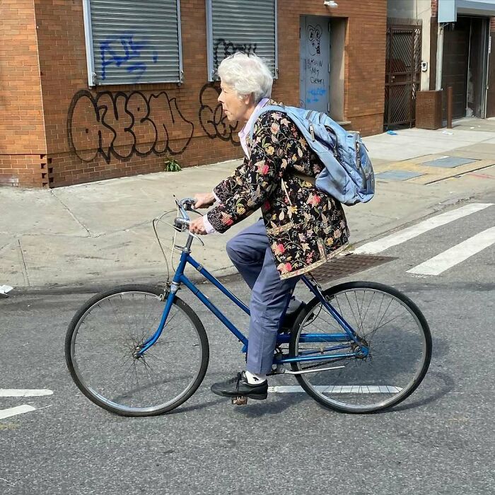 Staršia žena na bicykli s batohom jazdí po meste popri tehlovej budove s graffiti.