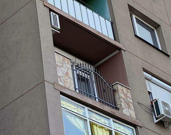 Balkón bez zábradlia s dekoratívnou kovovou bránou na bytovom dome, vedľa klimatizačnej jednotky.