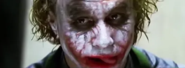 Osoba s výrazným make-upom a rozcuchanými vlasmi, výrazné farby na tvári, temný pohľad.