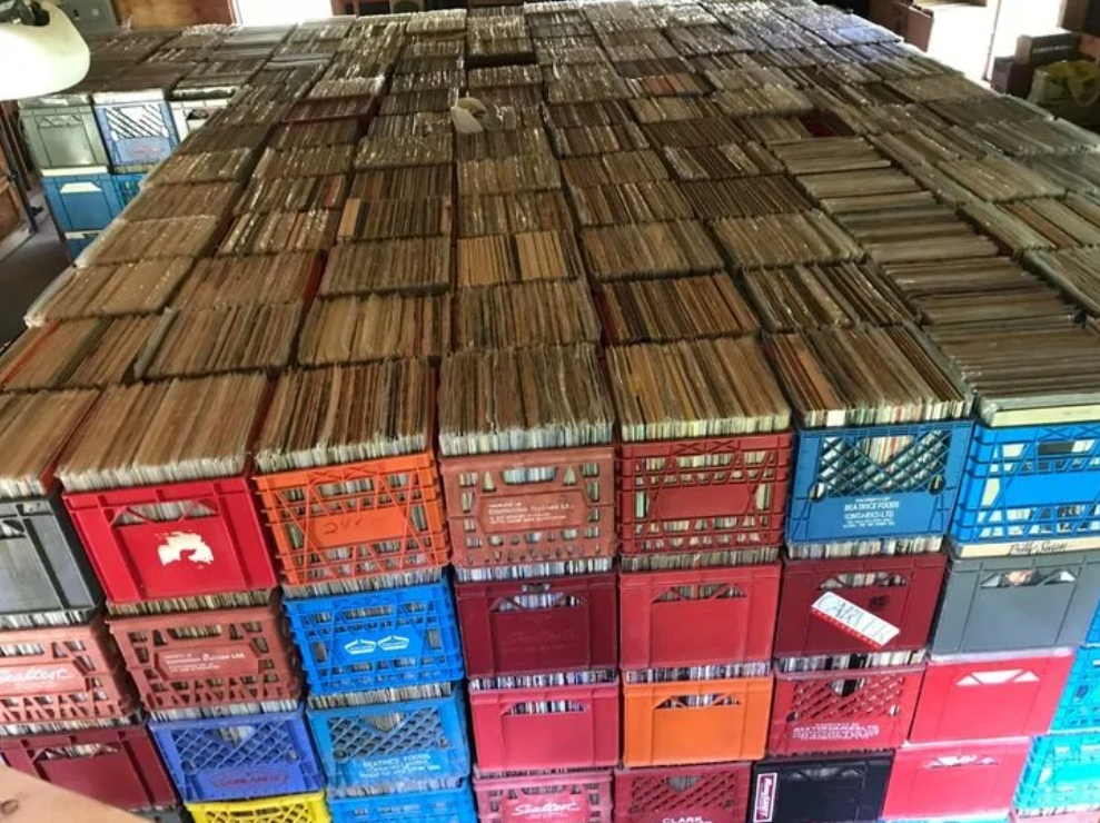 Stovky vinylových platní uložené v plastových debničkách, usporiadané v miestnosti na drevenom stole.