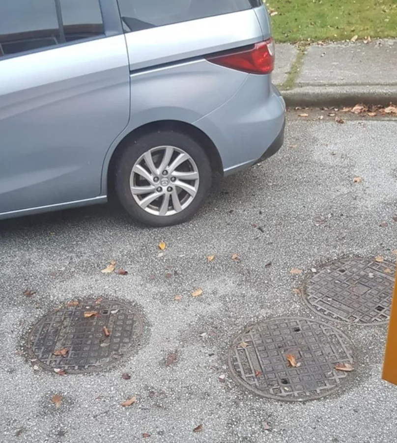 Auto zaparkované vedľa troch kanálových poklopov na ulici, podzimné lístie na zemi.