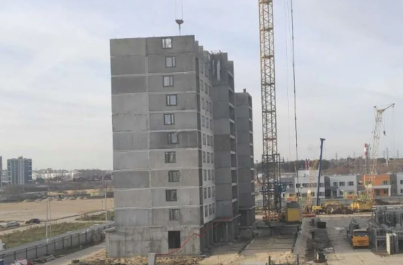 Rozostavaná bytovka so žeriavmi na stavenisku, moderné mestské budovy v pozadí.