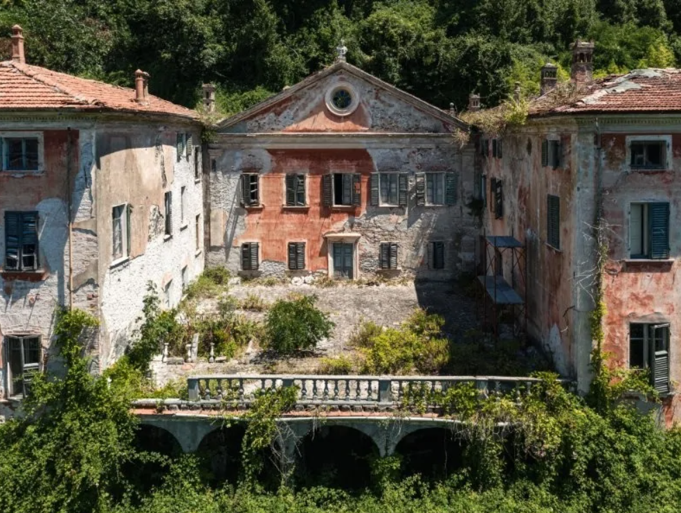 Opustená historická vila s obrastenou fasádou a rozpadnutým exteriérom, obklopená prírodou.