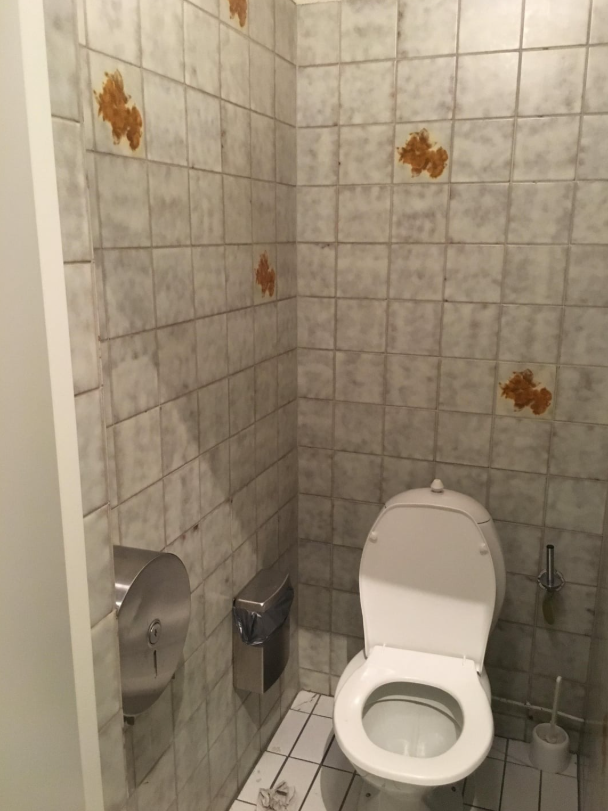 Toaleta s bielym WC, dlaždicami na stenách a dávkovačom papiera, čistý a funkčný priestor.