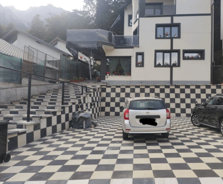 Auto na šachovnicovej dlažbe pred moderným domom s hory v pozadí, moderná architektúra a jedinečný dizajn.
