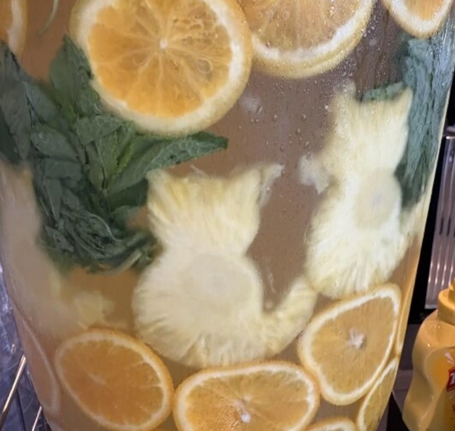 Osviežujúca citrusová voda s plátkami pomaranča, ananásu a lístkami mäty vo veľkej nádobe.