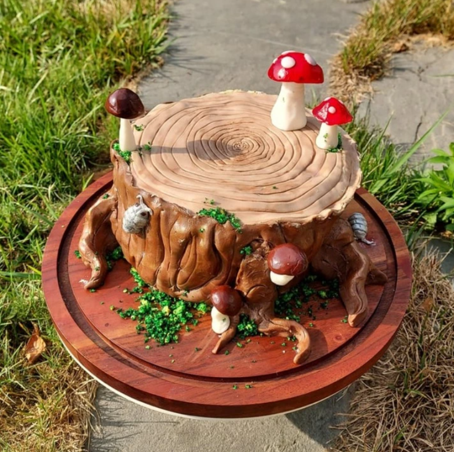 Torta v tvare pňa s hríbikmi a machom, detailné cukrárske umenie na drevenom podnose.