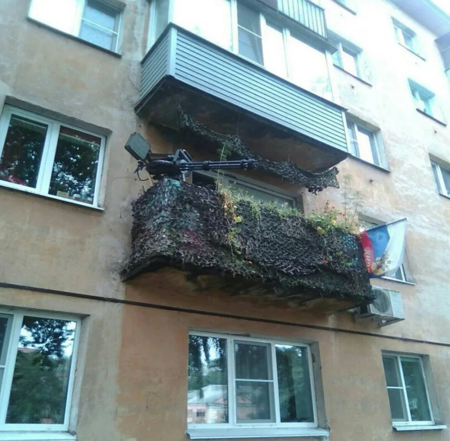 Balkón zdobený maskovacou sieťou a replikou zbrane na obytnej budove.